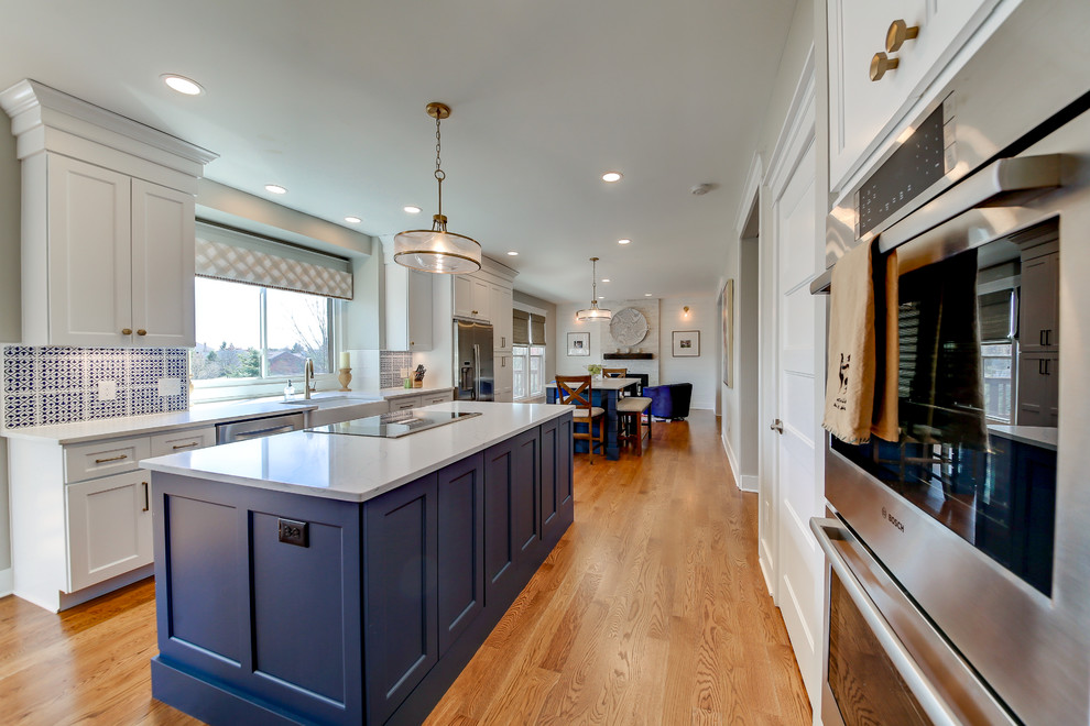 Example of a large transitional galley light wood floor and brown floor open concept kitchen design in Dallas with a farmhouse sink, recessed-panel cabinets, blue cabinets, quartzite countertops, multicolored backsplash, cement tile backsplash, stainless steel appliances, two islands and white countertops