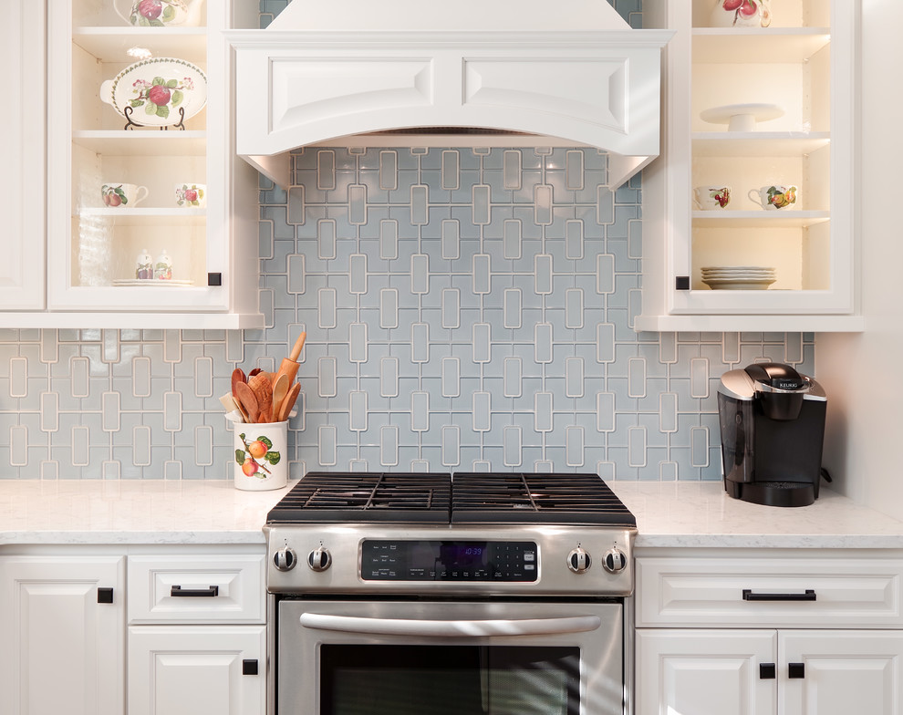 Mid-sized transitional u-shaped medium tone wood floor and brown floor eat-in kitchen photo with a farmhouse sink, raised-panel cabinets, white cabinets, quartz countertops, blue backsplash, porcelain backsplash, paneled appliances and an island