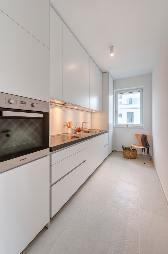 Photo of a small contemporary single-wall separate kitchen in Cologne with a drop-in sink, flat-panel cabinets, white cabinets, granite benchtops, stainless steel appliances, cement tiles, no island and beige floor.