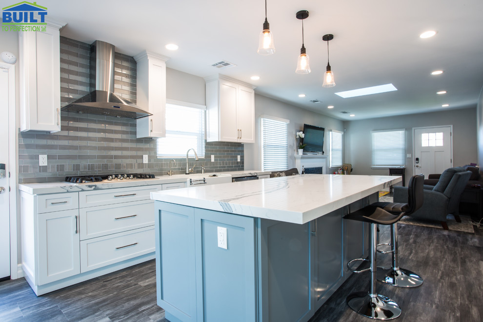 Photo of a mid-sized transitional single-wall open plan kitchen in Los Angeles with a farmhouse sink, shaker cabinets, white cabinets, marble benchtops, grey splashback, glass tile splashback, stainless steel appliances, ceramic floors, with island, grey floor and white benchtop.