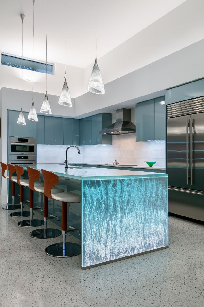 Mid-sized modern galley open plan kitchen in Tampa with an undermount sink, flat-panel cabinets, blue cabinets, glass benchtops, white splashback, ceramic splashback, stainless steel appliances, terrazzo floors, with island, multi-coloured floor and blue benchtop.