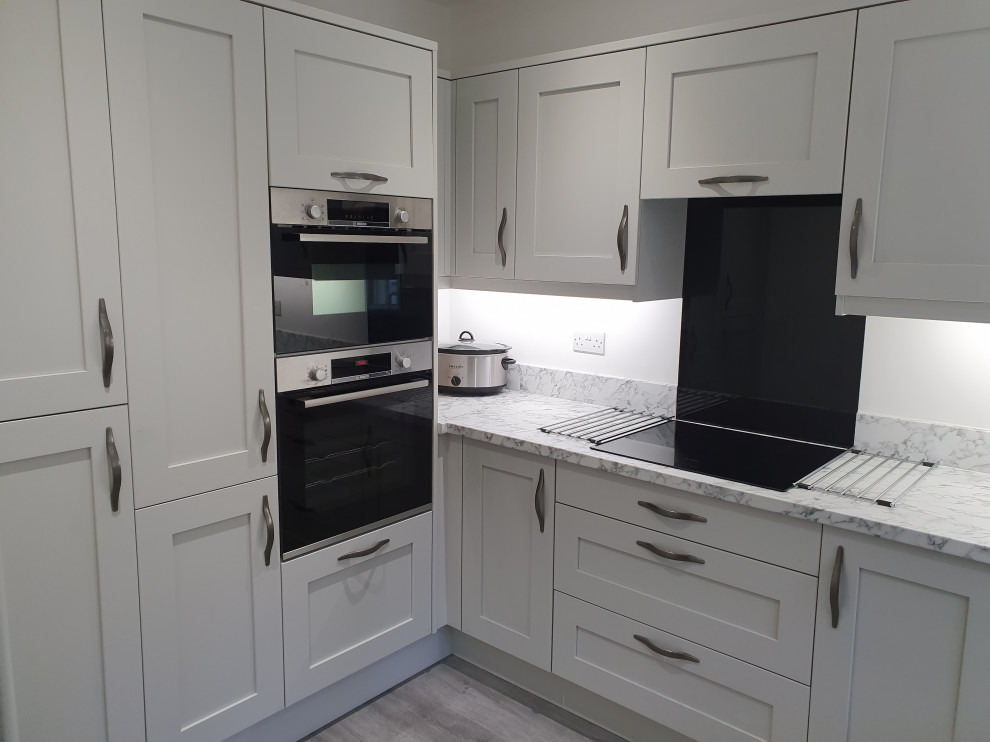 This is an example of a small contemporary u-shaped separate kitchen in West Midlands with a double-bowl sink, shaker cabinets, grey cabinets, laminate benchtops, grey splashback, glass tile splashback, black appliances, laminate floors, no island, grey floor and grey benchtop.