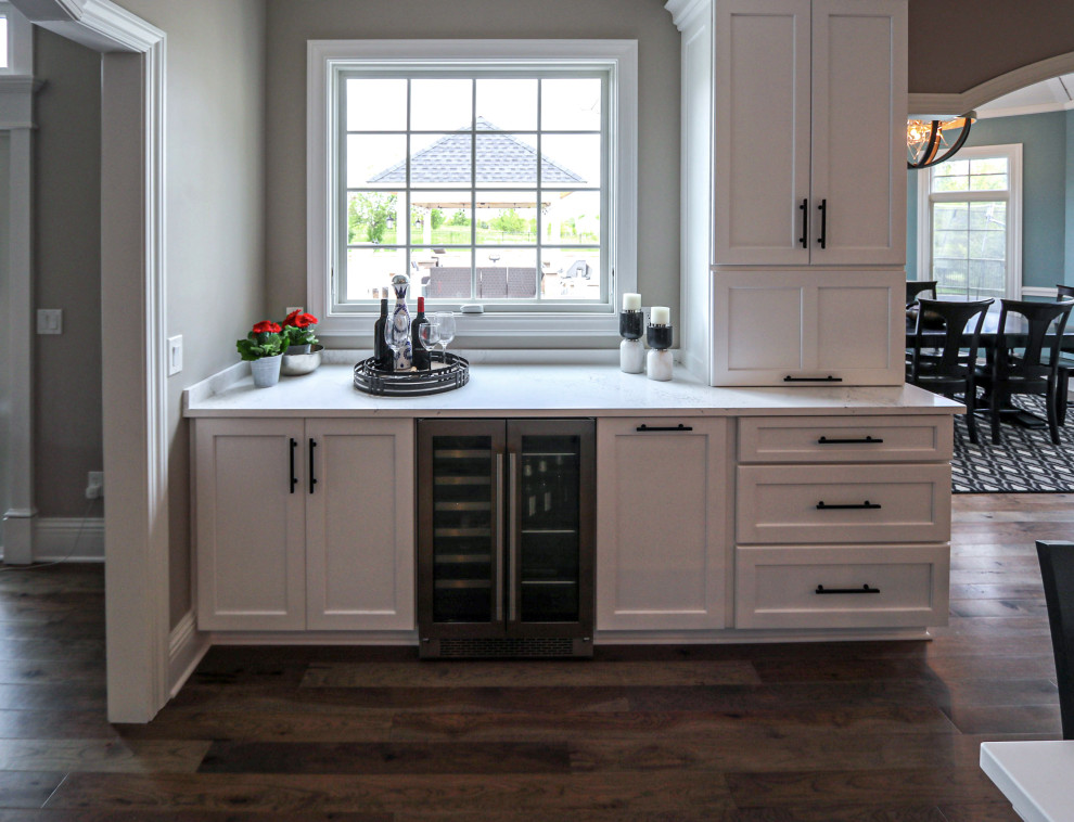 Bild på ett stort vintage vit vitt kök, med en undermonterad diskho, släta luckor, vita skåp, bänkskiva i kvarts, grått stänkskydd, stänkskydd i glaskakel, rostfria vitvaror, mellanmörkt trägolv, en köksö och beiget golv