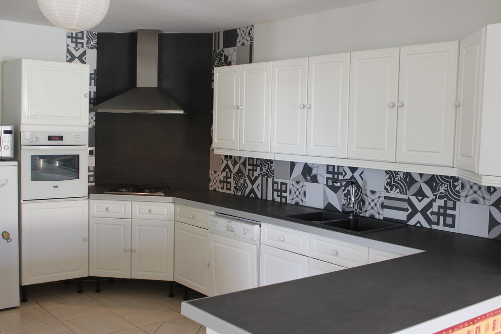 Photo of a mid-sized midcentury l-shaped eat-in kitchen in Montpellier with an integrated sink, flat-panel cabinets, white cabinets, laminate benchtops, multi-coloured splashback, cement tile splashback, panelled appliances, porcelain floors, with island, beige floor and black benchtop.