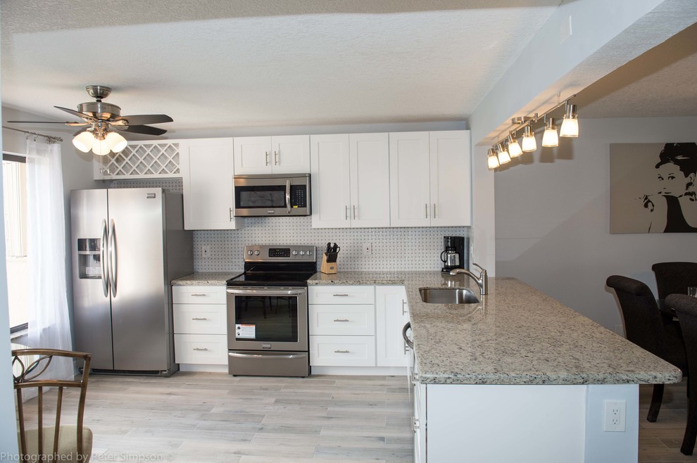 Photo of a mid-sized contemporary l-shaped separate kitchen in Miami with an undermount sink, shaker cabinets, white cabinets, granite benchtops, white splashback, mosaic tile splashback, stainless steel appliances, ceramic floors, a peninsula and grey floor.