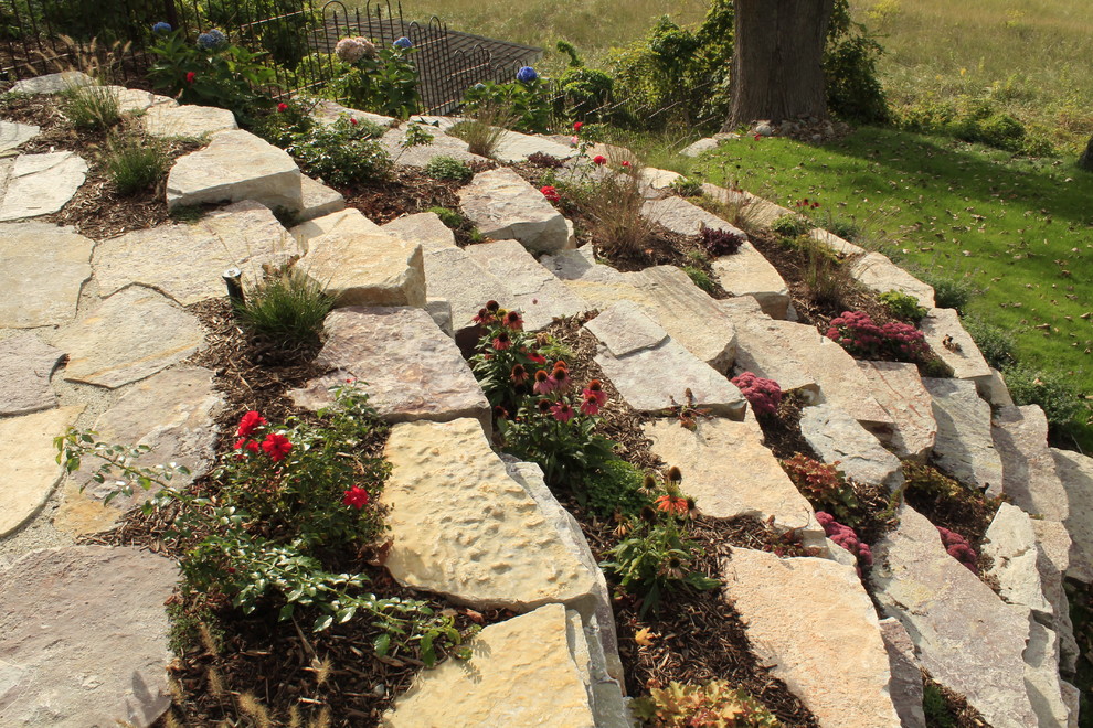 Photo of a large country sloped full sun xeriscape for summer in Grand Rapids with a retaining wall and natural stone pavers.