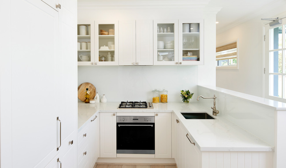 Small transitional u-shaped kitchen in Sydney with an undermount sink, white cabinets, white splashback, glass sheet splashback, no island, white floor, white benchtop and raised-panel cabinets.