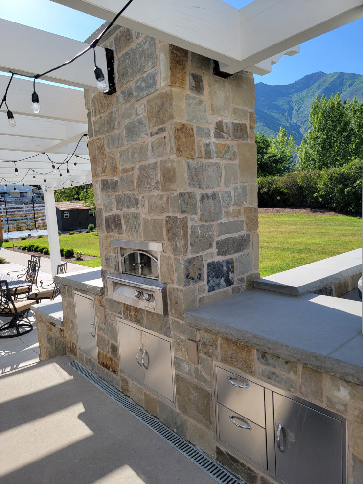 Large back patio in Salt Lake City with an outdoor kitchen, concrete slabs and a pergola.