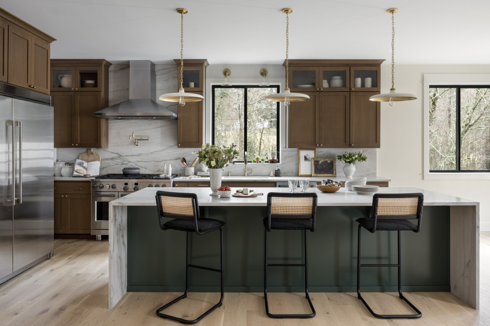 Open concept kitchen - large transitional l-shaped light wood floor and beige floor open concept kitchen idea in Seattle with a farmhouse sink, shaker cabinets, green cabinets, quartzite countertops, gray backsplash, stone slab backsplash, stainless steel appliances, an island and gray countertops