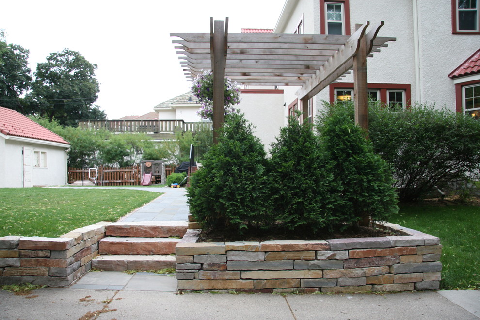 Large arts and crafts front yard shaded driveway in Minneapolis with a retaining wall and natural stone pavers.