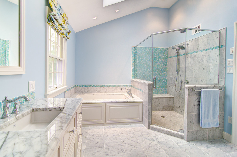 Photo of a large traditional master bathroom in Philadelphia with an undermount sink, raised-panel cabinets, white cabinets, marble benchtops, an undermount tub, a corner shower, a one-piece toilet, white tile, stone tile, blue walls and marble floors.