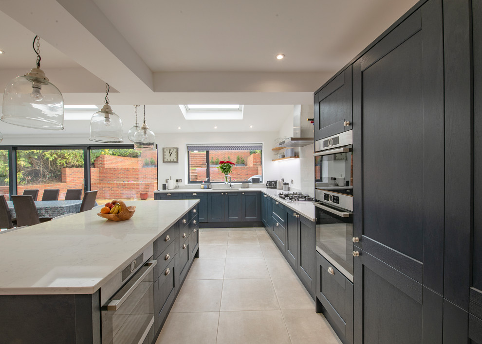 Expansive transitional l-shaped eat-in kitchen in Surrey with an undermount sink, shaker cabinets, blue cabinets, panelled appliances, porcelain floors, with island, beige floor and grey benchtop.