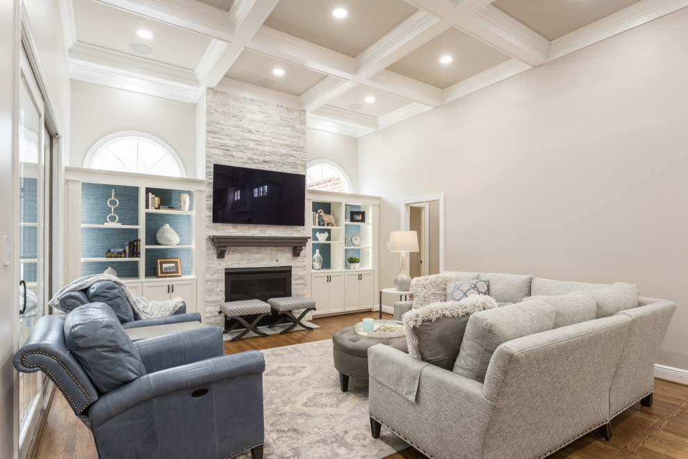 This is an example of a large traditional open plan living room in Raleigh with grey walls, medium hardwood flooring, a standard fireplace, a stacked stone fireplace surround, a built-in media unit and a coffered ceiling.