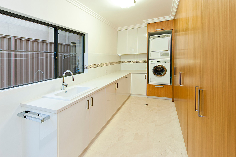Design ideas for a mid-sized modern u-shaped utility room in Perth with a drop-in sink, recessed-panel cabinets, medium wood cabinets, marble benchtops, white walls, marble floors and a stacked washer and dryer.