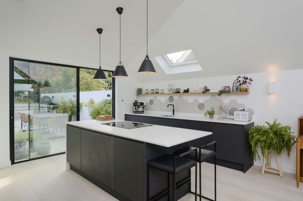 Foto på ett stort funkis vit kök med öppen planlösning, med en integrerad diskho, släta luckor, svarta skåp, bänkskiva i koppar, grått stänkskydd, stänkskydd i keramik, svarta vitvaror, ljust trägolv och en köksö