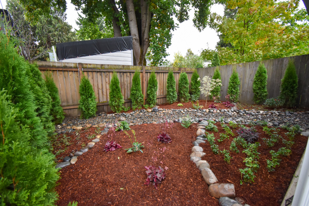 Photo of a mid-sized front yard full sun garden for fall in Portland with with rock feature, river rock and a wood fence.