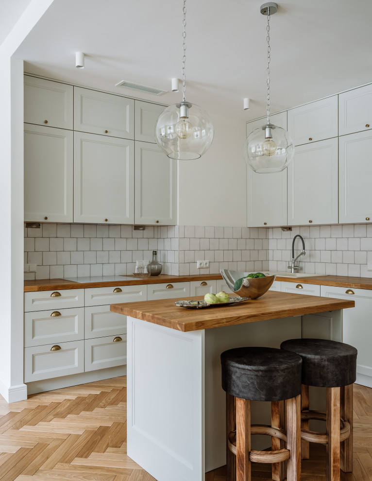 Photo of a scandinavian l-shaped kitchen in Moscow with a drop-in sink, recessed-panel cabinets, white cabinets, wood benchtops, white splashback, light hardwood floors, with island, beige floor and brown benchtop.