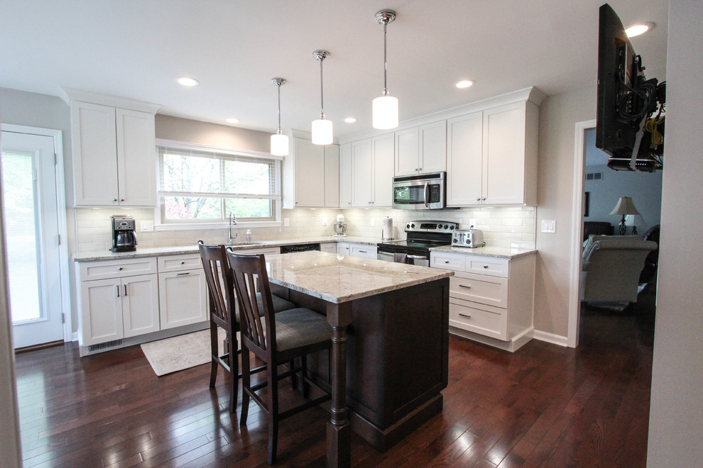 Enclosed kitchen - mid-sized transitional l-shaped dark wood floor and brown floor enclosed kitchen idea in Cincinnati with an undermount sink, shaker cabinets, white cabinets, granite countertops, beige backsplash, porcelain backsplash, stainless steel appliances, an island and white countertops