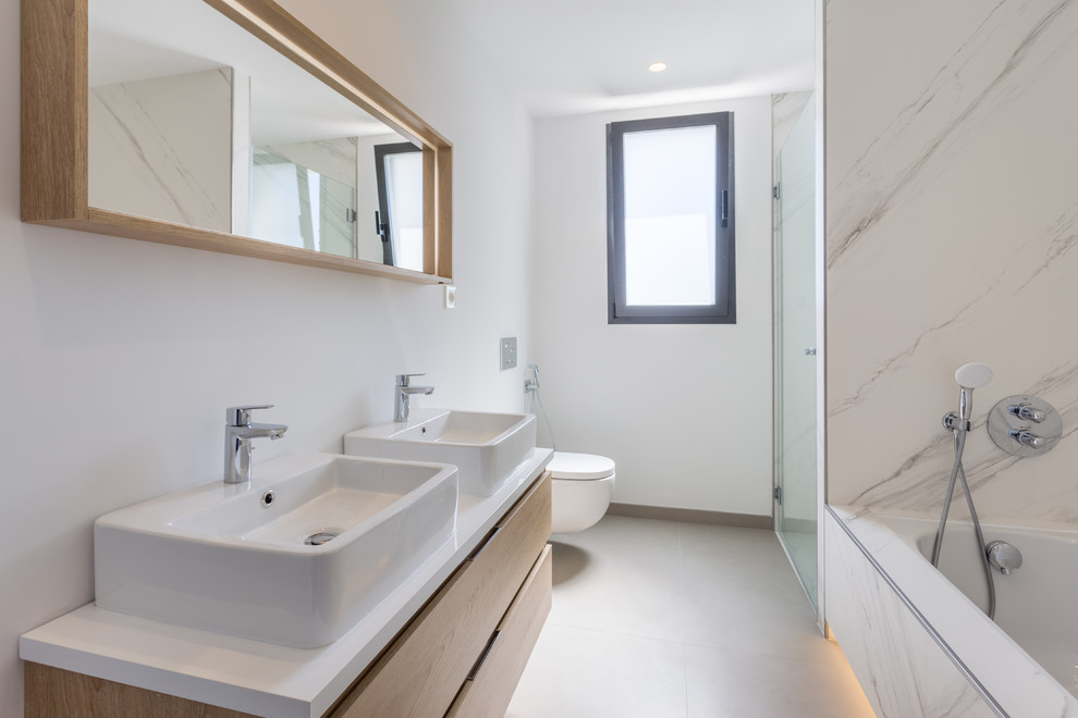 Mid-sized contemporary 3/4 wet room bathroom in Other with light wood cabinets, a wall-mount toilet, white tile, ceramic tile, white walls, ceramic floors, a vessel sink, wood benchtops, a hinged shower door, white benchtops, flat-panel cabinets, an undermount tub and beige floor.