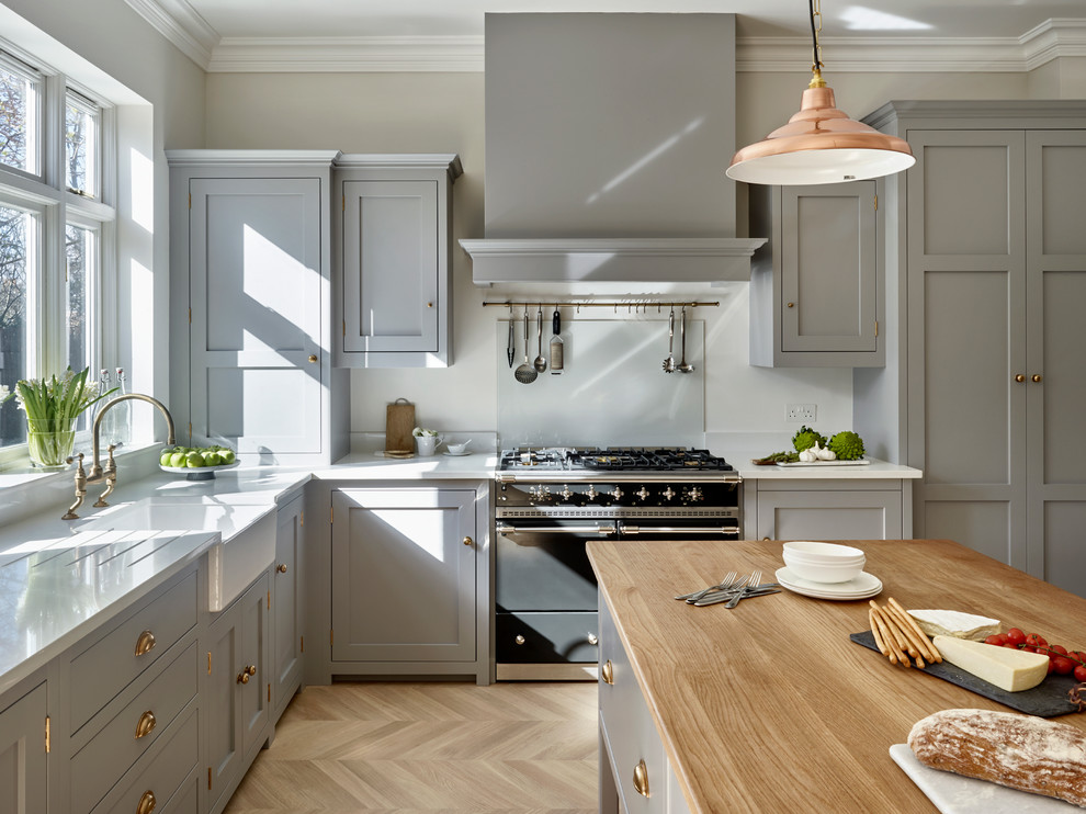 This is an example of a transitional l-shaped eat-in kitchen in London with a farmhouse sink, grey cabinets, light hardwood floors, with island and shaker cabinets.