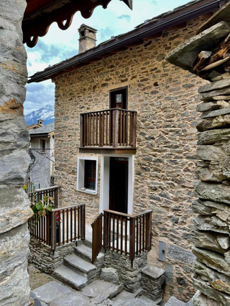 Foto della villa piccola beige rustica a quattro piani con rivestimento in pietra, tetto a capanna, tetto grigio e terreno in pendenza