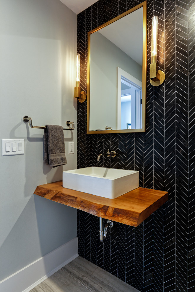 Mid-sized contemporary powder room in Cincinnati with black tile, a vessel sink, wood benchtops, grey floor, grey walls, brown benchtops, porcelain tile and porcelain floors.