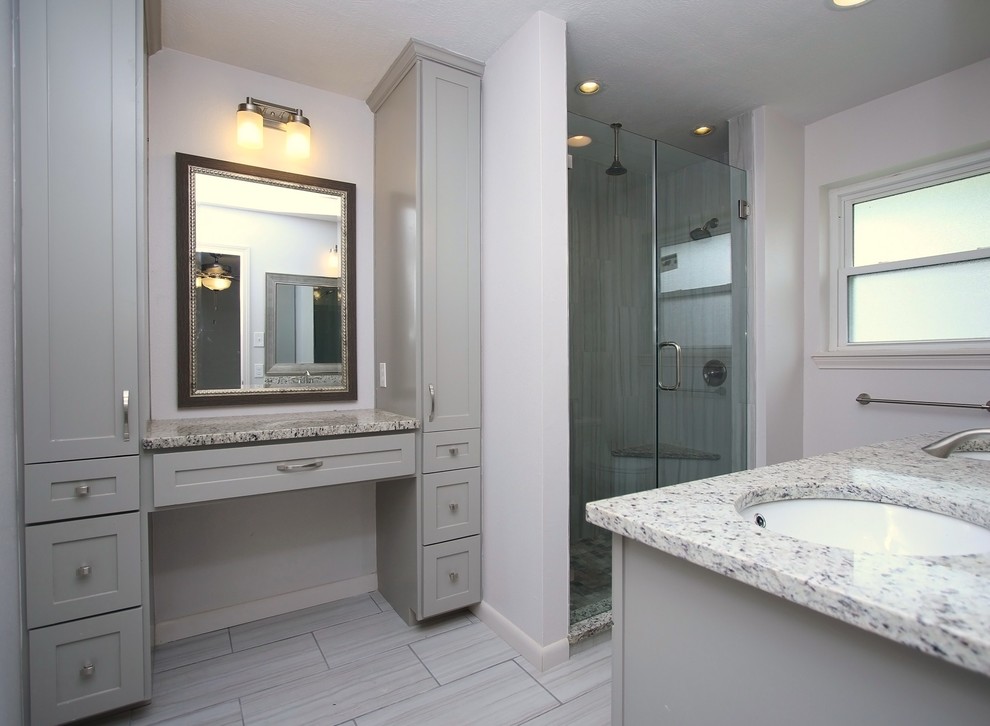 Photo of a mid-sized transitional master bathroom in Houston with shaker cabinets, grey cabinets, a two-piece toilet, gray tile, porcelain tile, grey walls, porcelain floors, an undermount sink, granite benchtops and a corner shower.