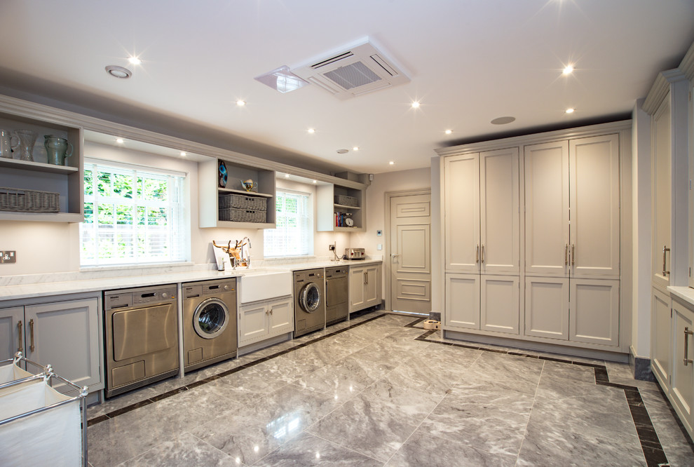 Transitional utility room in Buckinghamshire with a farmhouse sink, recessed-panel cabinets, grey cabinets, marble benchtops, white walls, marble floors, a side-by-side washer and dryer, grey floor and white benchtop.