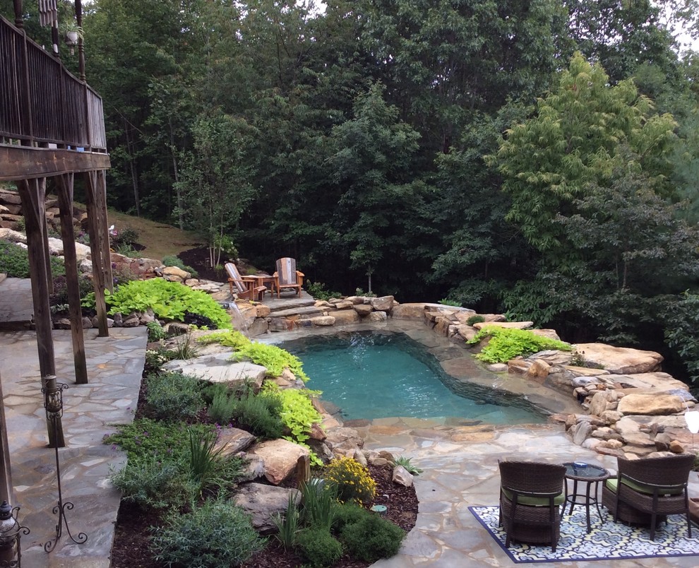 This is an example of a mid-sized tropical backyard custom-shaped natural pool in Other with a water feature and natural stone pavers.