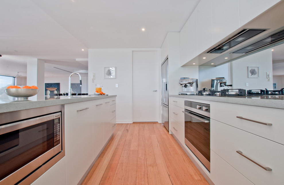 Photo of a mid-sized modern galley open plan kitchen in Sydney with an undermount sink, flat-panel cabinets, beige cabinets, quartzite benchtops, mirror splashback, stainless steel appliances, light hardwood floors and with island.