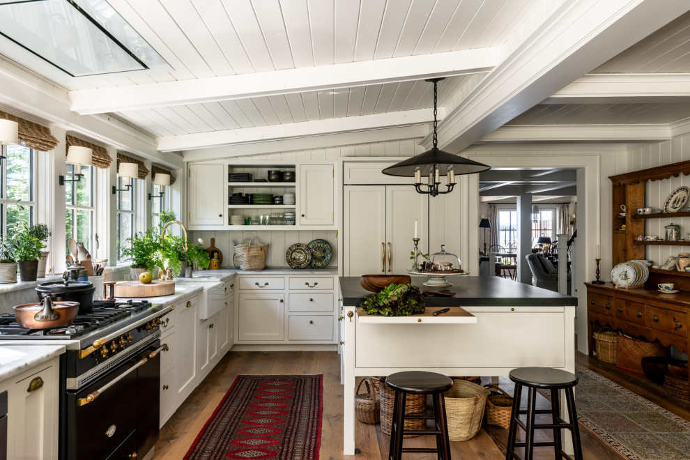 Traditional l-shaped kitchen in Seattle with a belfast sink, shaker cabinets, white cabinets, white splashback, integrated appliances, medium hardwood flooring, an island, brown floors, grey worktops, exposed beams, a timber clad ceiling and a vaulted ceiling.