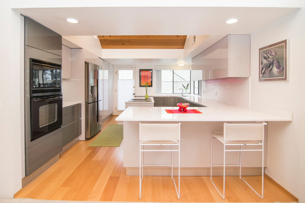 Design ideas for a mid-sized modern u-shaped separate kitchen in San Diego with an undermount sink, flat-panel cabinets, grey cabinets, quartz benchtops, white splashback, porcelain splashback, black appliances, light hardwood floors, with island and brown floor.