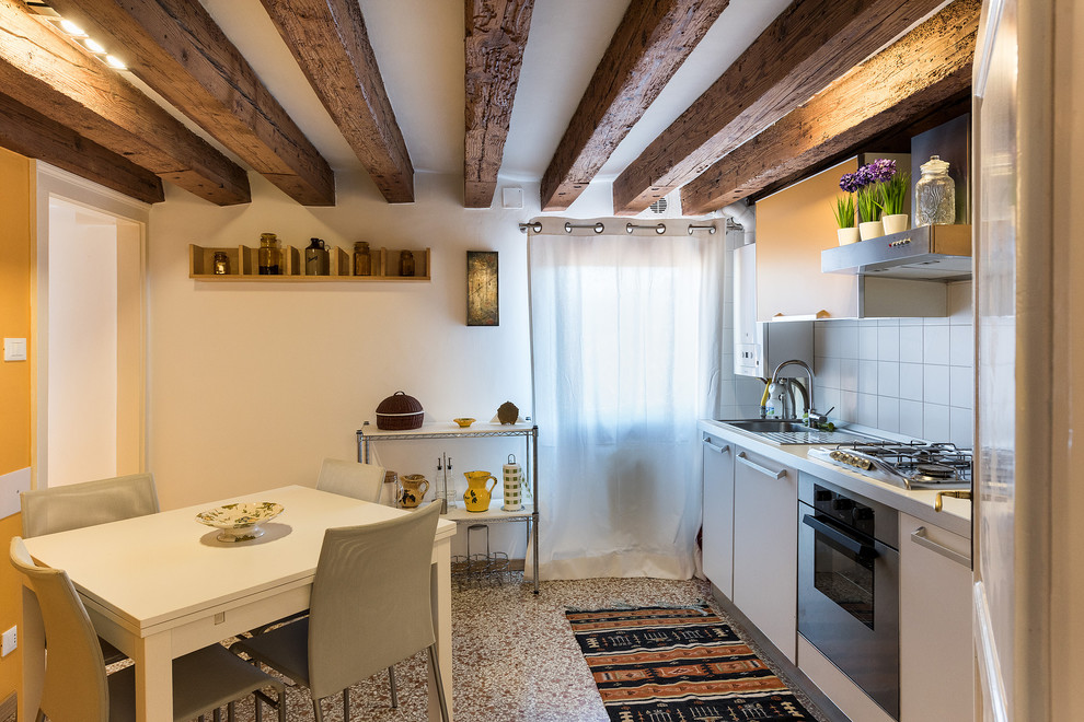 This is an example of a small country single-wall eat-in kitchen in Venice with flat-panel cabinets, white cabinets, white splashback, no island, a drop-in sink, stainless steel appliances and multi-coloured floor.