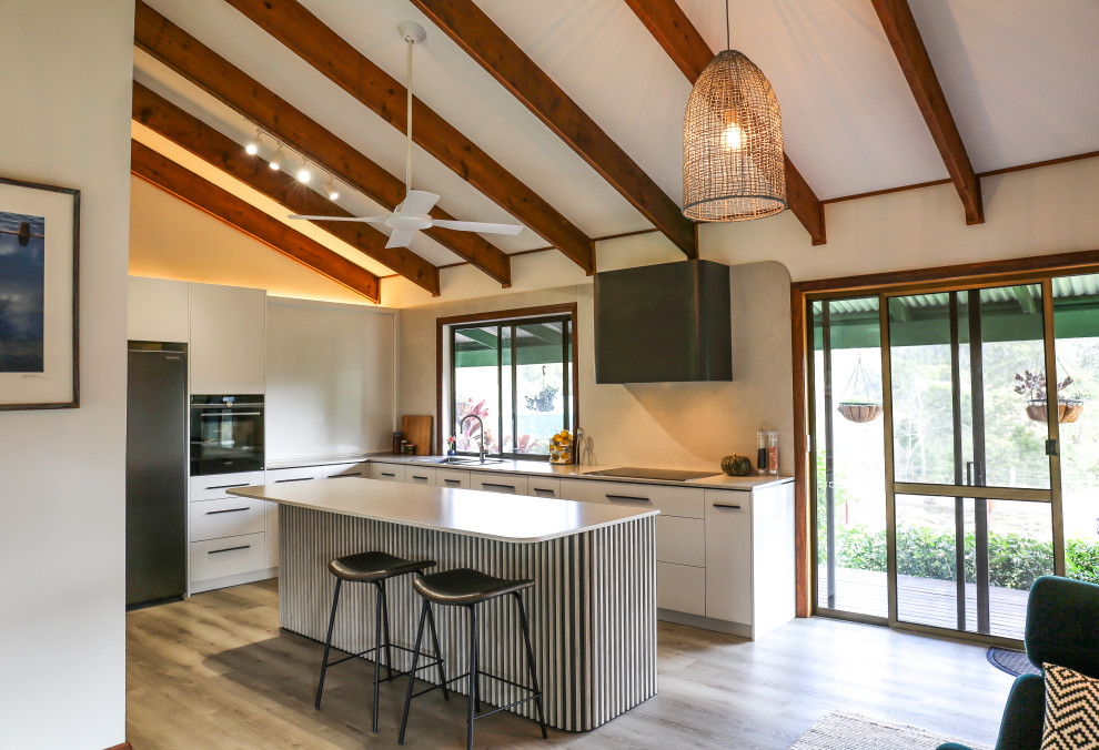 This is an example of a large contemporary l-shaped eat-in kitchen with a double-bowl sink, flat-panel cabinets, white cabinets, quartz benchtops, multi-coloured splashback, engineered quartz splashback, black appliances, laminate floors, with island, brown floor, multi-coloured benchtop and exposed beam.