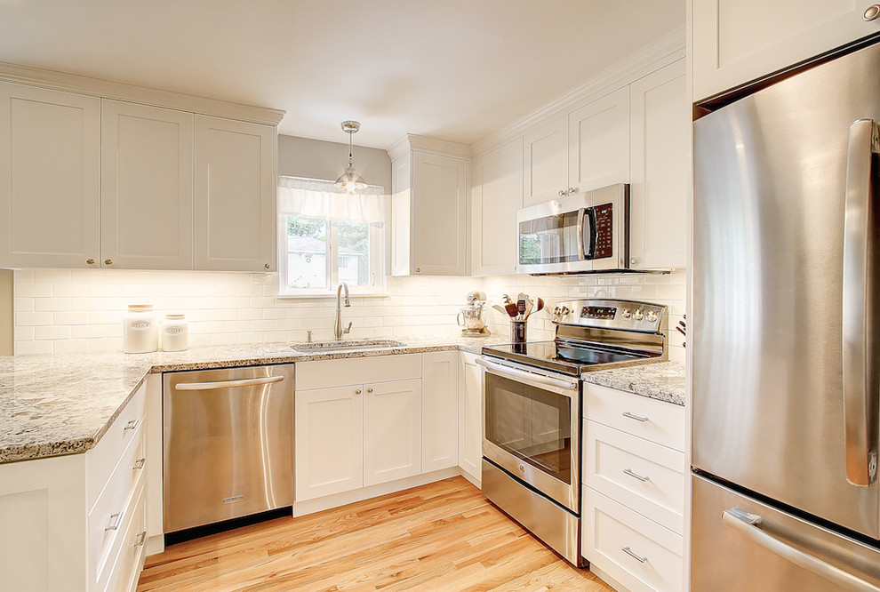Small contemporary u-shaped kitchen pantry in Seattle with an undermount sink, shaker cabinets, white cabinets, white splashback, subway tile splashback, stainless steel appliances, light hardwood floors, a peninsula and granite benchtops.
