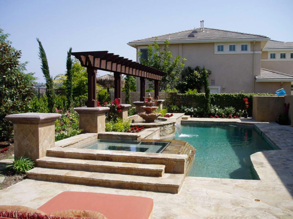 Photo of a large mediterranean backyard custom-shaped natural pool in Orange County with a hot tub and stamped concrete.