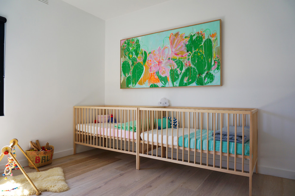 Photo of a contemporary gender-neutral nursery in Melbourne with white walls and light hardwood floors.