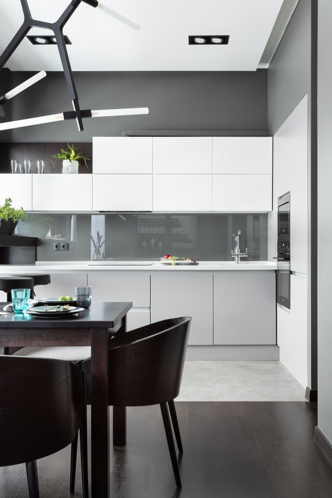 Design ideas for a mid-sized contemporary l-shaped open plan kitchen in Moscow with an integrated sink, flat-panel cabinets, white cabinets, solid surface benchtops, grey splashback, glass tile splashback, black appliances, porcelain floors, no island, grey floor and white benchtop.