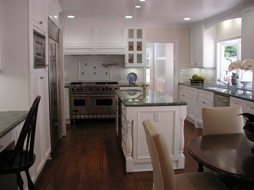Photo of a mid-sized traditional u-shaped eat-in kitchen in Los Angeles with an undermount sink, recessed-panel cabinets, white cabinets, granite benchtops, white splashback, subway tile splashback, stainless steel appliances, dark hardwood floors and with island.