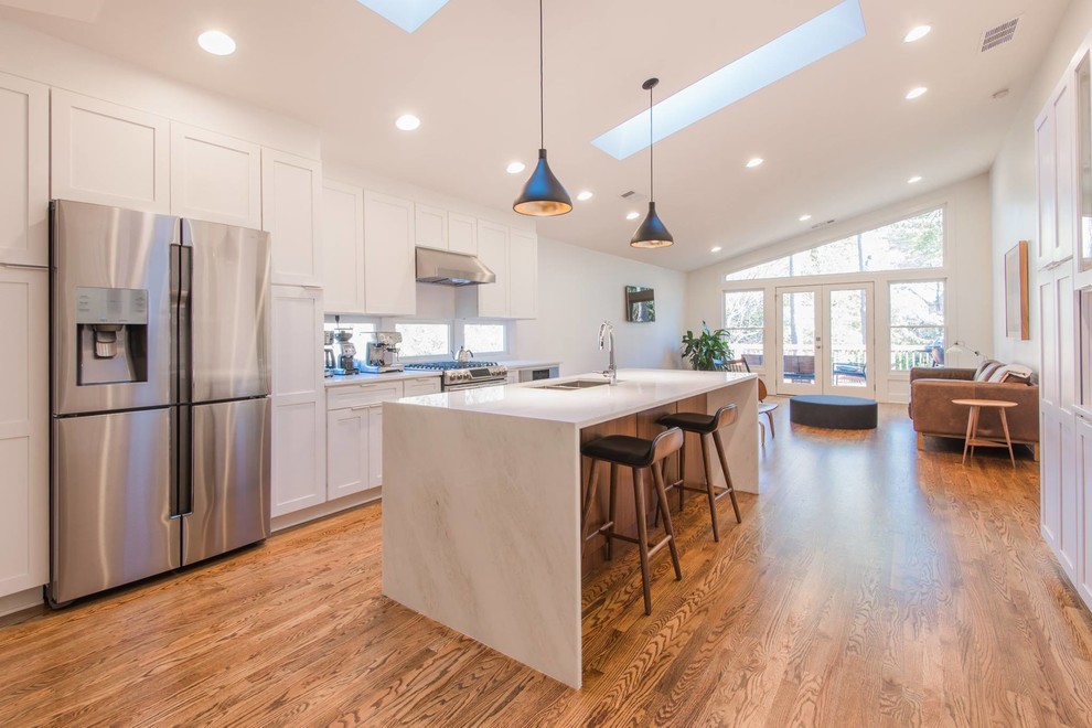 Open concept kitchen - mid-sized transitional single-wall light wood floor open concept kitchen idea in Atlanta with a double-bowl sink, recessed-panel cabinets, white cabinets, marble countertops, white backsplash, subway tile backsplash, stainless steel appliances and an island