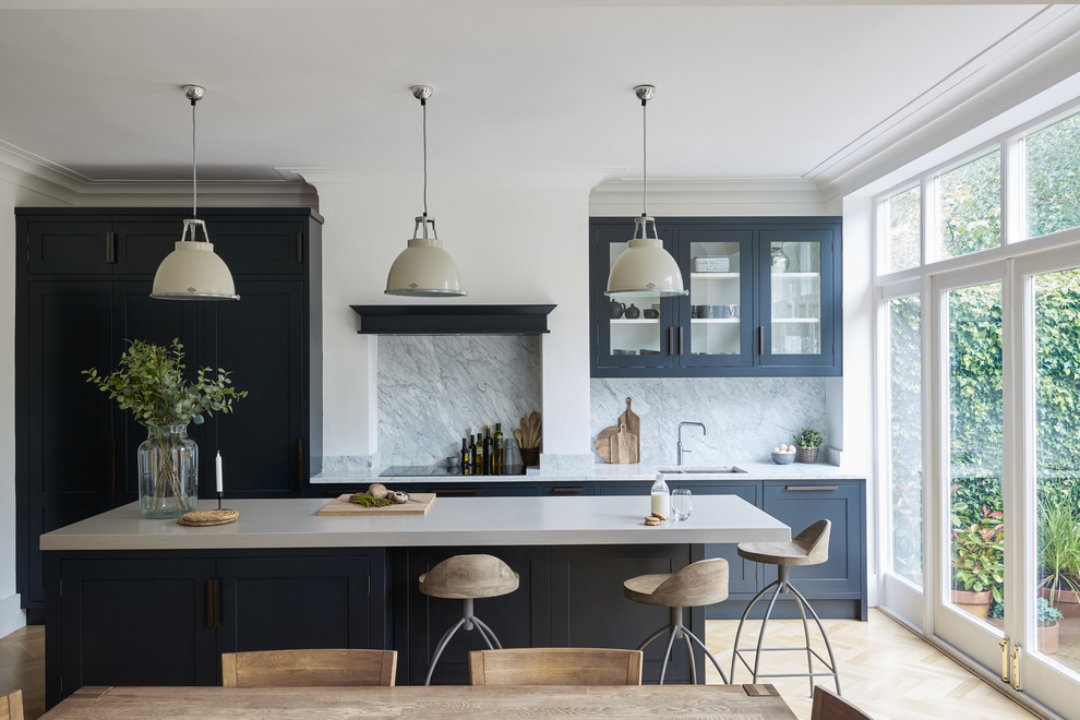 Large country galley eat-in kitchen in London with an integrated sink, shaker cabinets, blue cabinets, concrete benchtops, white splashback, marble splashback, panelled appliances, light hardwood floors, with island, beige floor and white benchtop.