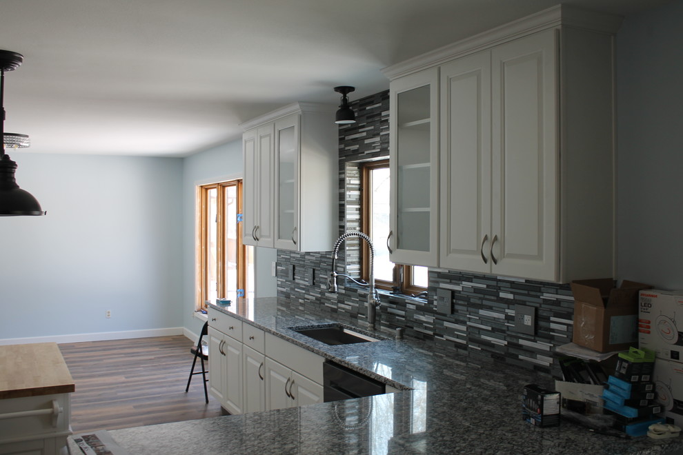 Example of a mid-sized transitional u-shaped dark wood floor and brown floor kitchen design with an undermount sink, raised-panel cabinets, white cabinets, granite countertops, multicolored backsplash, matchstick tile backsplash, stainless steel appliances and an island
