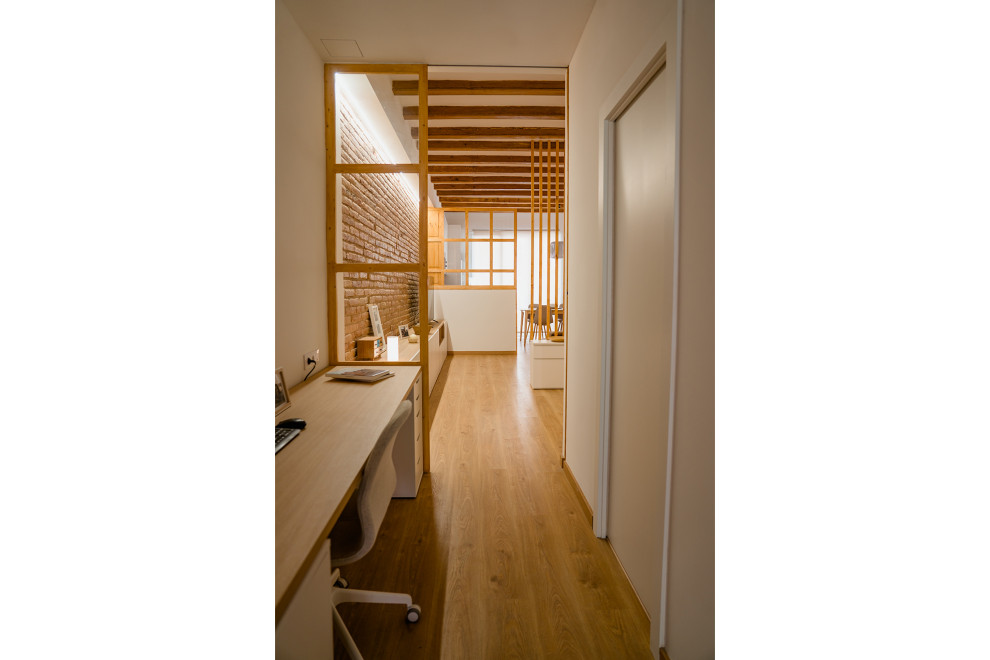 Mittelgroßes Uriges Arbeitszimmer mit Arbeitsplatz, weißer Wandfarbe, braunem Holzboden, Einbau-Schreibtisch, braunem Boden, freigelegten Dachbalken und Ziegelwänden in Barcelona