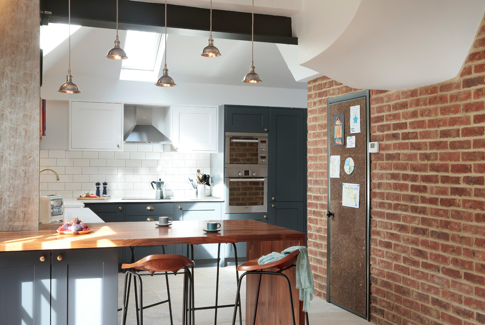 Inspiration for a mid-sized industrial u-shaped kitchen in London with shaker cabinets, blue cabinets, white splashback, stainless steel appliances, a peninsula, white benchtop, beige floor and subway tile splashback.