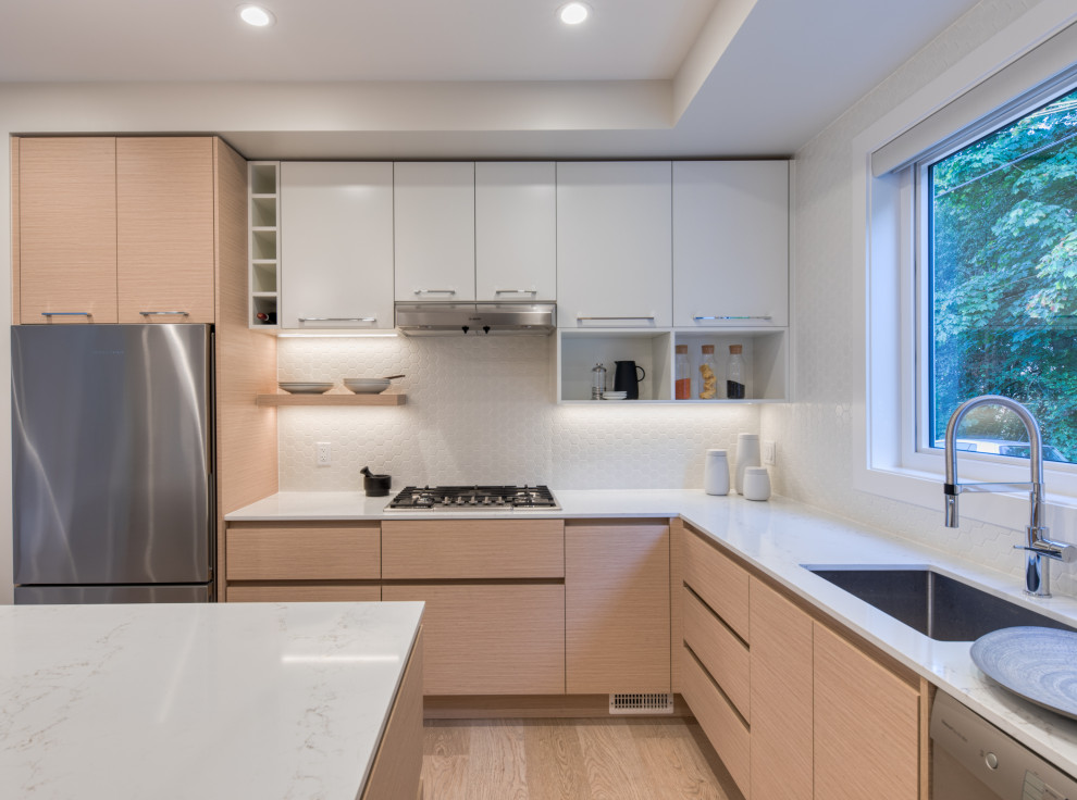 This is an example of a mid-sized modern l-shaped open plan kitchen in Vancouver with an undermount sink, flat-panel cabinets, light wood cabinets, marble benchtops, white splashback, ceramic splashback, stainless steel appliances, light hardwood floors, with island, beige floor and white benchtop.