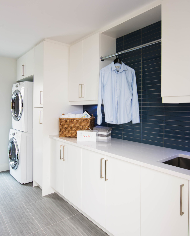 Photo of a mid-sized scandinavian single-wall utility room in Toronto with an undermount sink, flat-panel cabinets, white cabinets, quartzite benchtops, white walls, porcelain floors and a stacked washer and dryer.