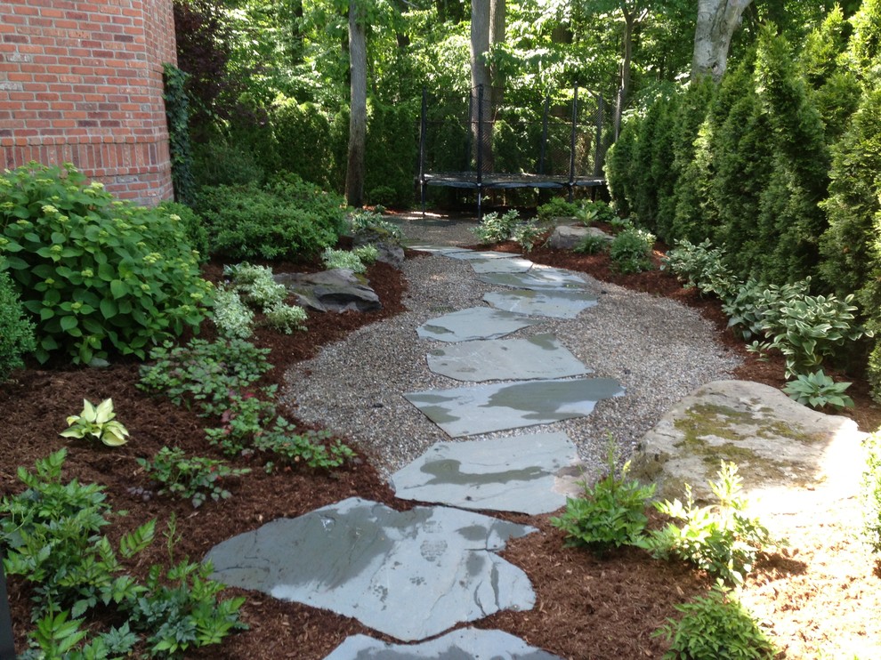 This is an example of a small country backyard shaded garden for fall in New York with a garden path and natural stone pavers.