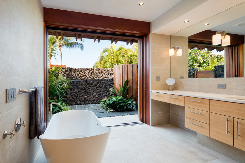 Tropical bathroom in Hawaii with flat-panel cabinets, medium wood cabinets, a freestanding tub, beige tile and an undermount sink.