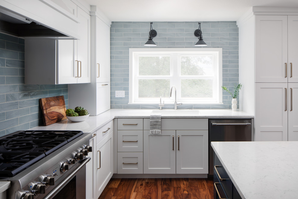 Mid-sized trendy l-shaped medium tone wood floor and brown floor open concept kitchen photo in Portland with an undermount sink, shaker cabinets, white cabinets, quartz countertops, blue backsplash, ceramic backsplash, stainless steel appliances, an island and white countertops