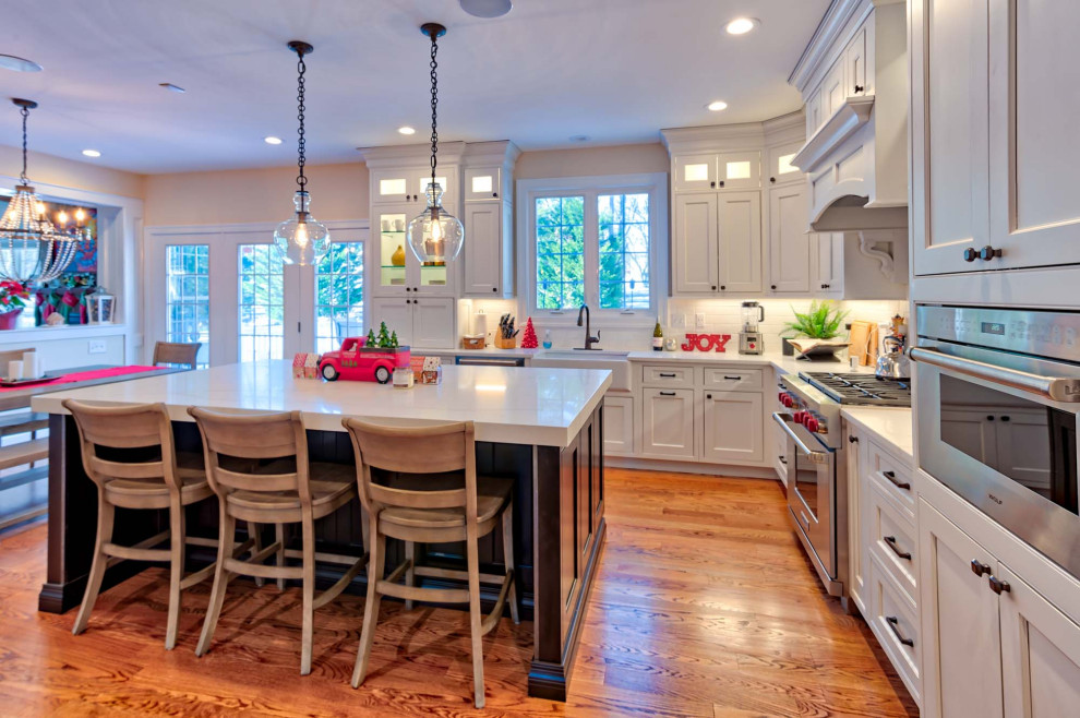 Inspiration for a large transitional l-shaped eat-in kitchen in Baltimore with a farmhouse sink, beaded inset cabinets, white cabinets, quartzite benchtops, white splashback, porcelain splashback, stainless steel appliances, medium hardwood floors, with island, brown floor and white benchtop.